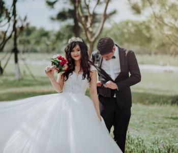 Woman in Wedding Dress Holding Flower With Man in Black Blazer