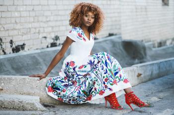 Woman in White and Multicolored Floral Flare Dress Sitting on Concrete