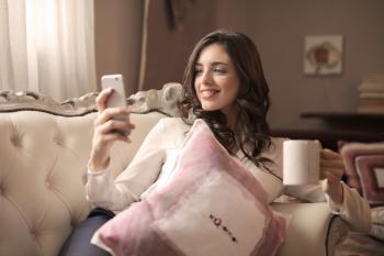Woman in White Long-sleeved Shirt Holding Smartphone Sitting on Tufted Sofa