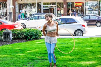 Woman in White Sleeveless Shirt and Blue Pants Holds Yellow Hula Hoop Stands on Green Grass