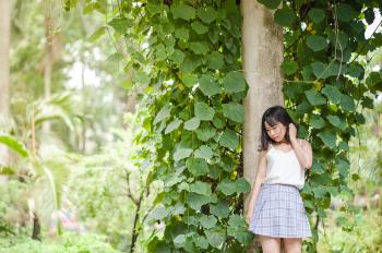 Woman in White Spaghetti Strap Top and Gray Skirt Standing in Front of Tree