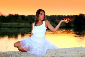 Woman in White Square Neckline Sleeveless Dress Sitting on Beige Wall Beside Body of Water during Golden Time