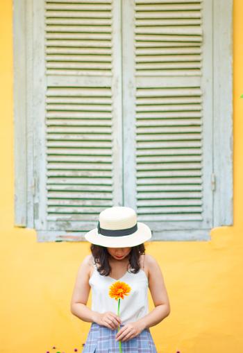 Woman in White Tank Top Holding Sunflower Near Window Outdoors