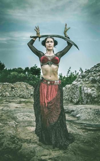 Woman Wearing Black and Red Dress Holding Sword Standing on Rock Surface during Day Time