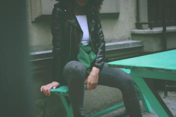 Woman Wearing Black Leather Jacket Sitting on Green Wooden Bench
