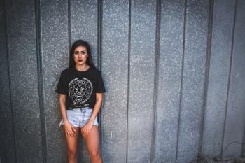 Woman Wearing Black Lion Graphic Crew-neck Shirt and Gray Denim Short Shorts Leaning on Gray Wall