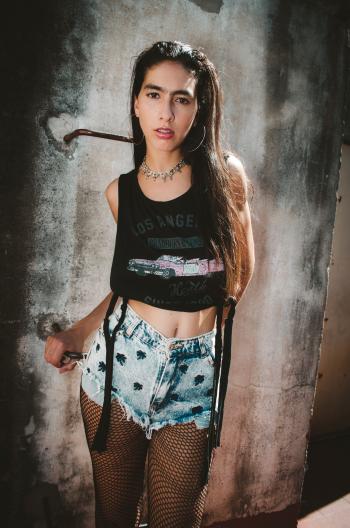 Woman Wearing Black Los Angeles Graphic Crop Top, Blue Denim Stonewashed Cut-off Short Shorts and Black Fishnet Stockings