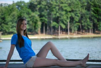 Woman Wearing Blue T Shirt and Beige Short Sitting on Brown Wooden Panel Near Body of Water during Daytime