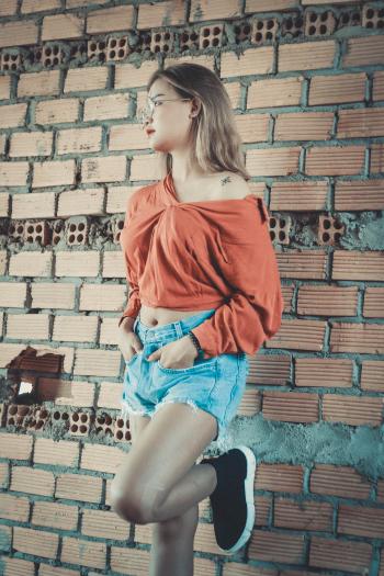 Woman Wearing Brown Long-sleeved Blouse and Blue Denim Short Shorts Standing Behind Brown Brick Wall