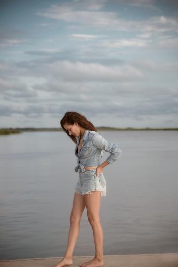 Woman Wearing Gray Denim Tie-front Long-sleeved Shirt and Short Shorts Walking on Isle Near Body of Water