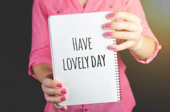 Woman Wearing Pink Dress Holding Graphing Notebook With Have a Lovely Day Sign