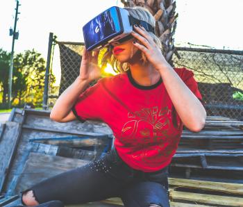 Woman Wearing Red and Black Top and Blue Distressed Bottoms Wearing Gray and Black Virtual Reality Sunglasses