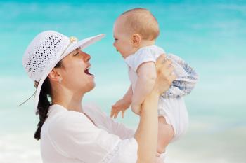Woman Wearing White Hat Holding Baby Wearing White Onesie Near Beach during Day Time