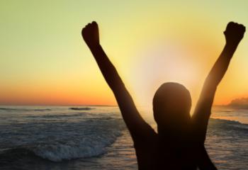 Woman with arms raised at sunset