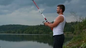 Young fisherman with a fishing rod on the shore of the lake in the ...