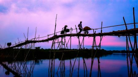 3 Person Walking on Bridge Under Cloudy Sky during Sunrise