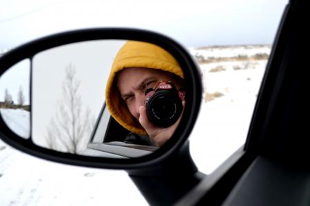 A man takes a photo through a car mirror
