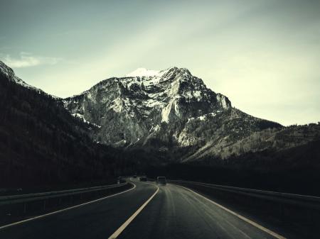 Asphalt Road With Running Vehicle Infront of Mountain Under Gray Sky