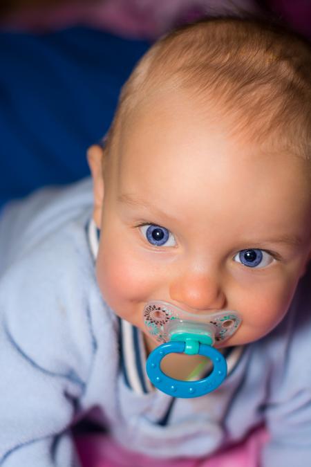 Baby on Blue Romper Biting Pacifier