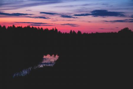 Body of Water Between Silhouette of Trees Under Red Black and Grey Sky at Sunset