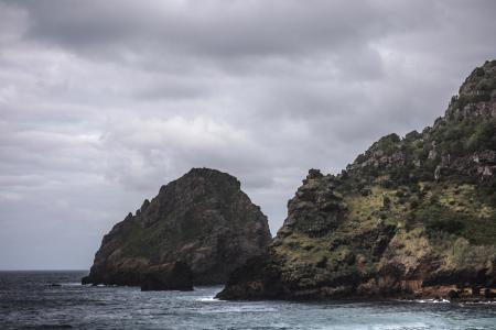 Brown Rock Formation on Body of Water Under Gray Clouds