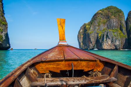 Brown Row Boat Sailing on Clear Body of Water in Between Rock Formations Under Clear Blue Sky