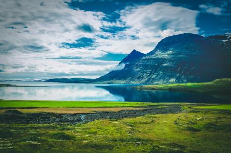 Calm Body of Water Near Black Mountain Surrounded by Green Grass