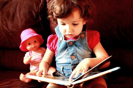 Child reading a book with doll