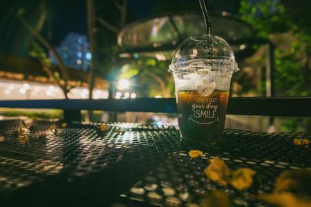 Clear Plastic Disposable Cup With Straw Half-filled With Juice on Metal Table