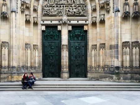 Couple Sitting on Ladders Outside Yellow Concrete Building With 2 Green Wooden Doors