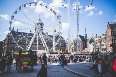 Ferris Wheel Beside Brown Buildings and People Under Blue Cloudy Sky at Daytime