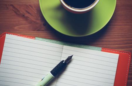 Fountain Pen on Top of Notebook Beside Drinking Mug