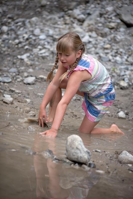 Girl in Pink White and Blue Romper in Body of Water With Gray Rocks
