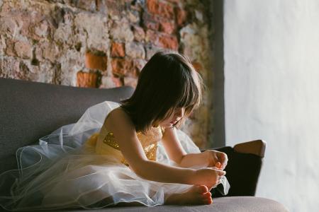 Girl in Yellow-and-white Dress Sitting on Couch While Holding Her Foot