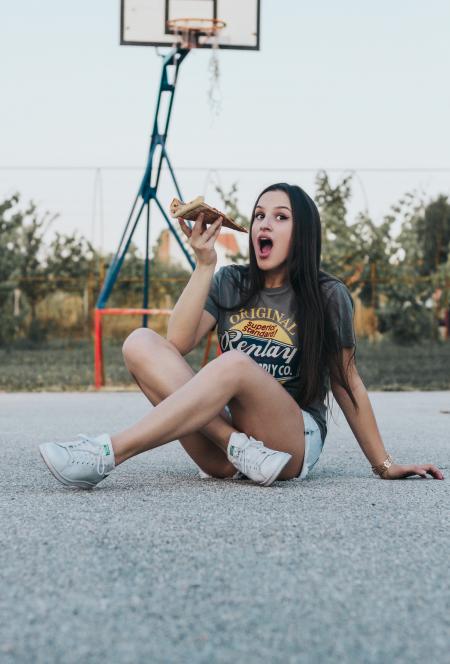 Girl Sitting on Basketball Field Holding Pizza