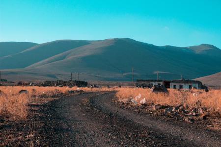 Gray Road in Between Brown Grass Field With Mountains Background