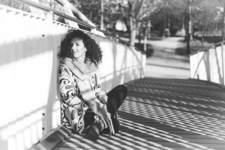 Grayscale Photo of a Woman Sitting Beside a Rail