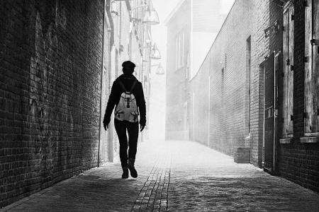 Grayscale Photo of Person Near Brick Wall