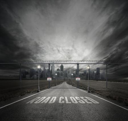 Grayscale Photo of Road Closed on Roadway With Gray Fence Gate in Front of City