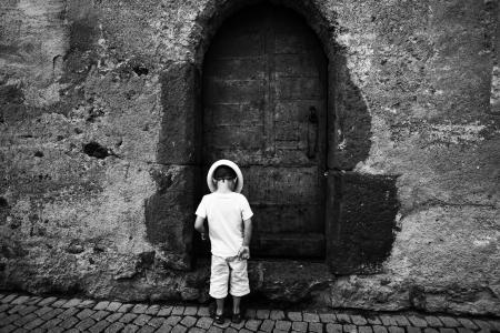 Grayscale Photo of Toddler Standing and Wearing Hat on the Ground