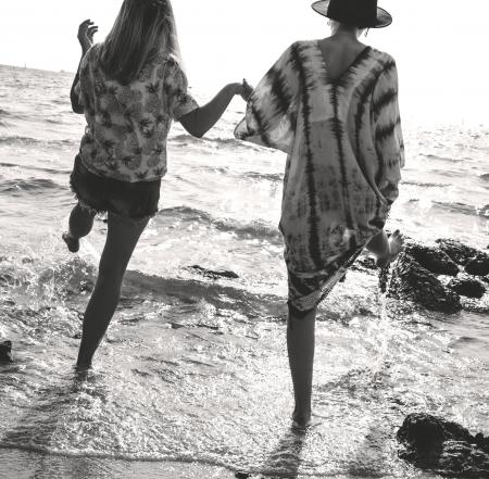 Grayscale Photograph of 2 Women Holding Hands While Walking on Sea Shore