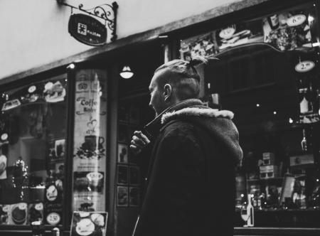 Grayscale Photograph of Man Walking Past by Shop
