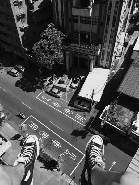 Grayscale Photography Man Wearing All Star Converse High Tops Below in Street and Building