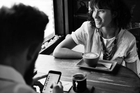 Grayscale Photography of Man and Woman Sitting Beside Wooden Table