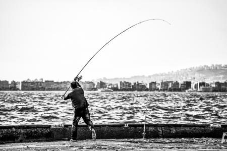 Grayscale Photography of Man Holding a Fishing Rod Near Body of Water