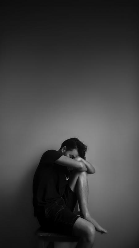 Grayscale Photography of Man Sitting Beside Wall