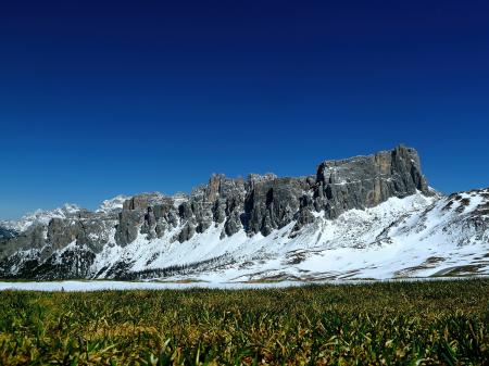 Green Fields Under Grey Rock Formations Covered With Snow