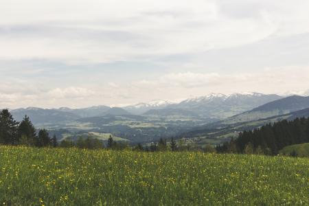 Green Grass Field Under Grey Clear Sky Overlooking Mountains