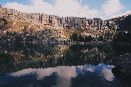 Grey Rocky Mountain Near Body of Water Under Blue Sky With White Clouds during Day Time