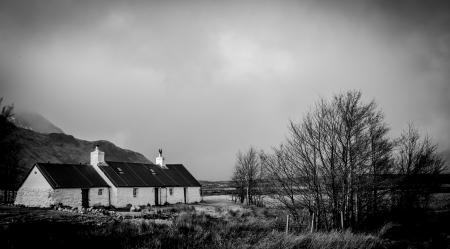 Greyscale Photo of House Within Mountain Range